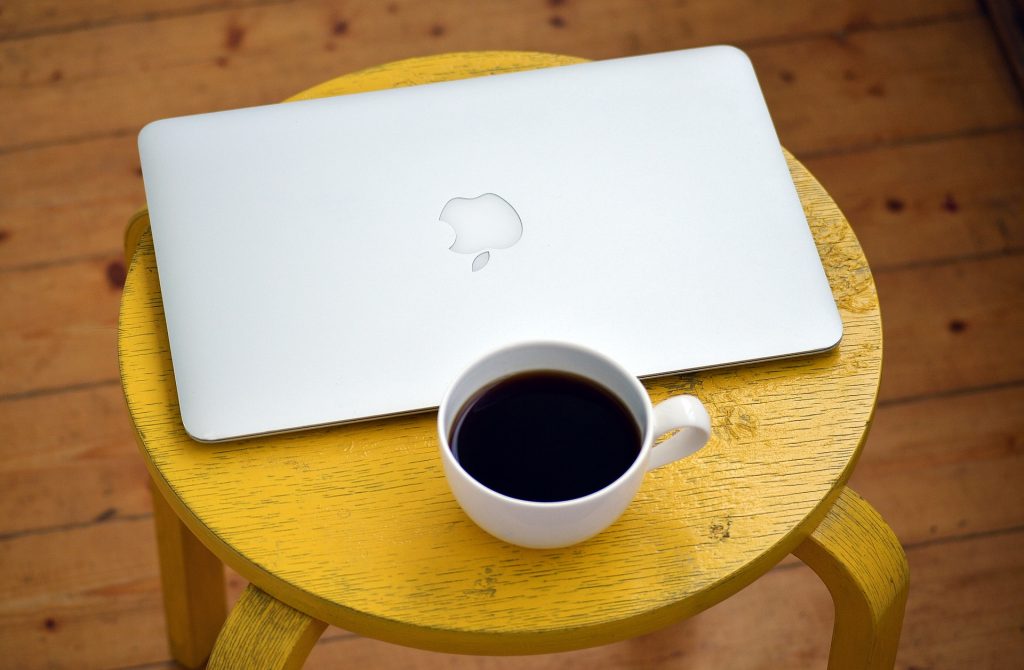 Computer and cup of coffee on yellow stool.
